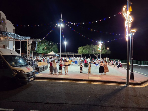 Baile de magos nocturno en San Isidro con personas vestidas con traje tradicional canario en una plaza decorada con luces festivas.