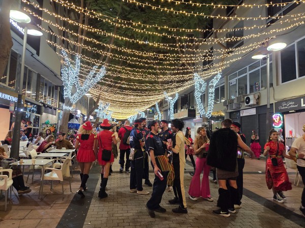 Ambiente del carnaval de Santa Cruz con personas disfrazadas caminando por una calle peatonal cubierta de luces decorativas.