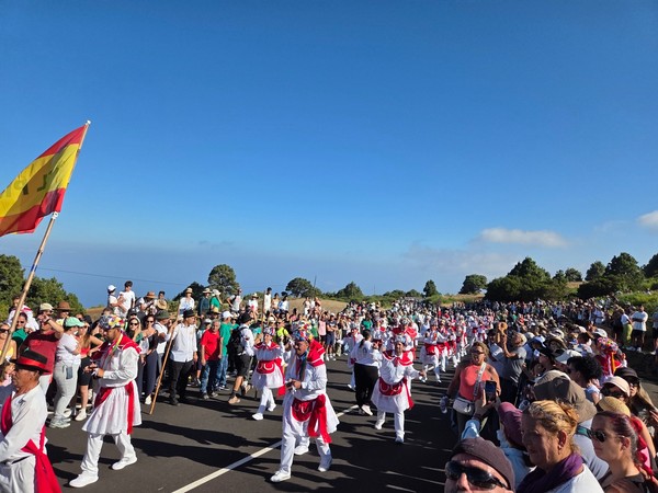 Romería o desfile popular en El Hierro con participantes vestidos de blanco y rojo avanzando entre una gran multitud.