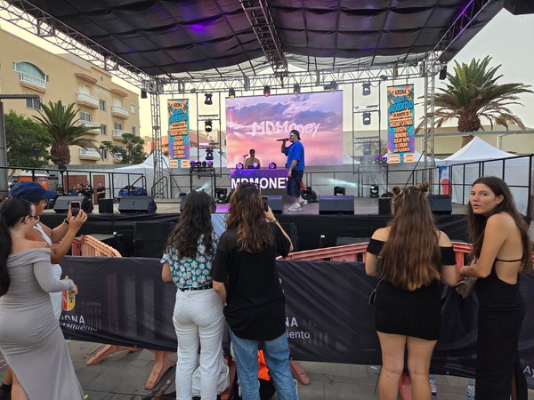 Festival juvenil en Las Galletas con un artista actuando en el escenario mientras varias personas observan desde la valla.