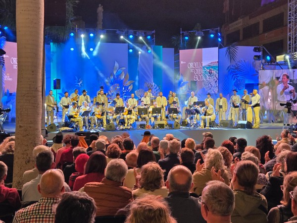Grupo folclórico actuando en un escenario al aire libre ante un público sentado durante un evento cultural nocturno.