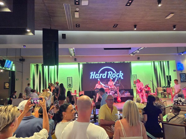 Concierto en el interior del Hard Rock con una banda tocando en el escenario y público cenando y mirando la actuación.