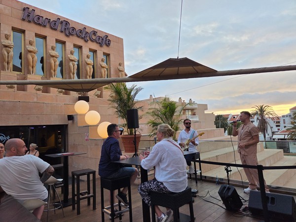 Actuación musical en la terraza del Hard Rock Café al atardecer, con cantante, guitarrista y mesas de clientes.