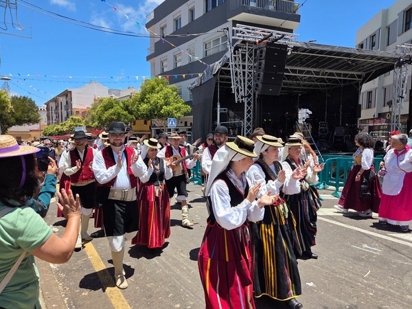 Desfile folclórico de San Benito Abad con participantes vestidos con trajes tradicionales canarios caminando y aplaudiendo junto a un escenario.